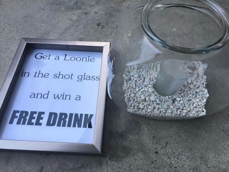 a glass jar filled with gravel next to a sign that says get a loonie in the shot glass and win a free drink