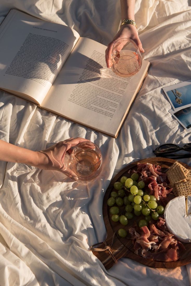 a person laying on a bed with an open book and glass of wine in their hand