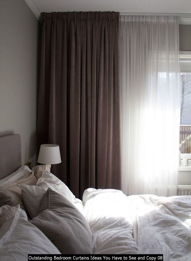 an unmade bed in front of a window with curtains