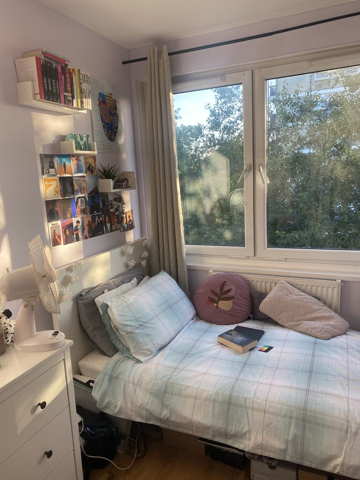 a small bedroom with a bed, dresser and window overlooking the trees in the distance