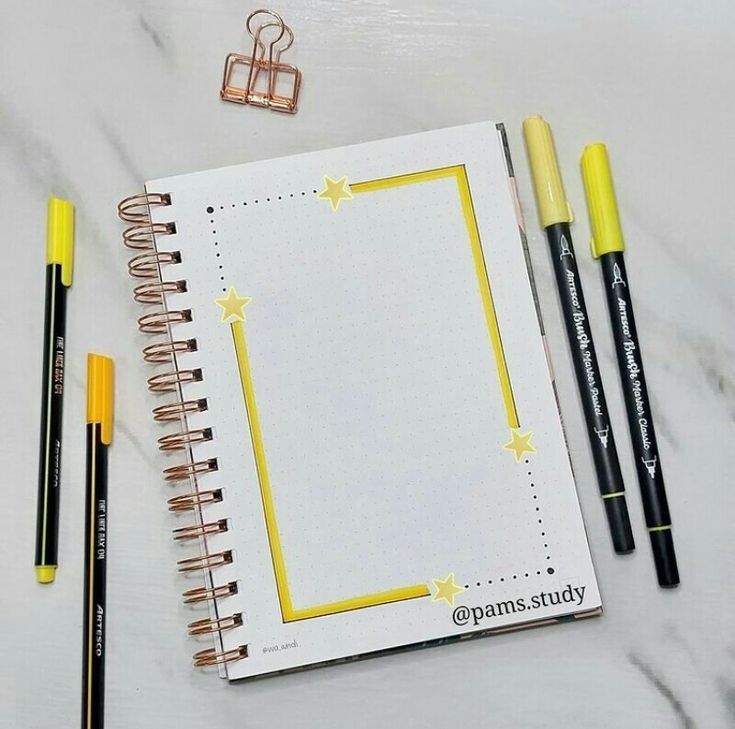 an open spiral notebook next to two pencils and a notepad on a marble surface