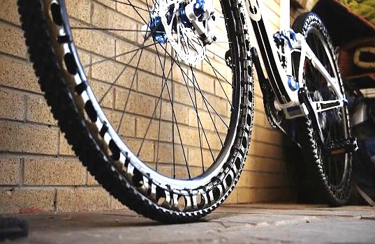 the front wheel of a bicycle parked next to a brick wall with wheels on it