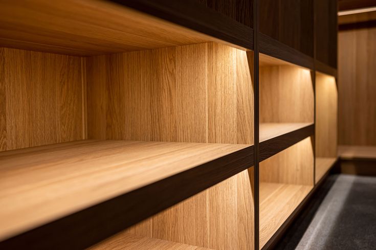 wooden shelves in a room with black flooring and lighting on the wall behind them