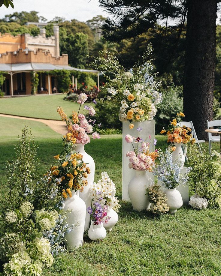 several white vases with flowers in them on the grass