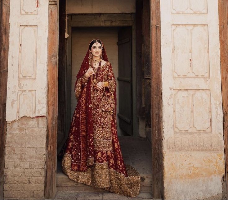 a woman in a red and gold bridal gown standing outside an open doorway with her hands on her hips