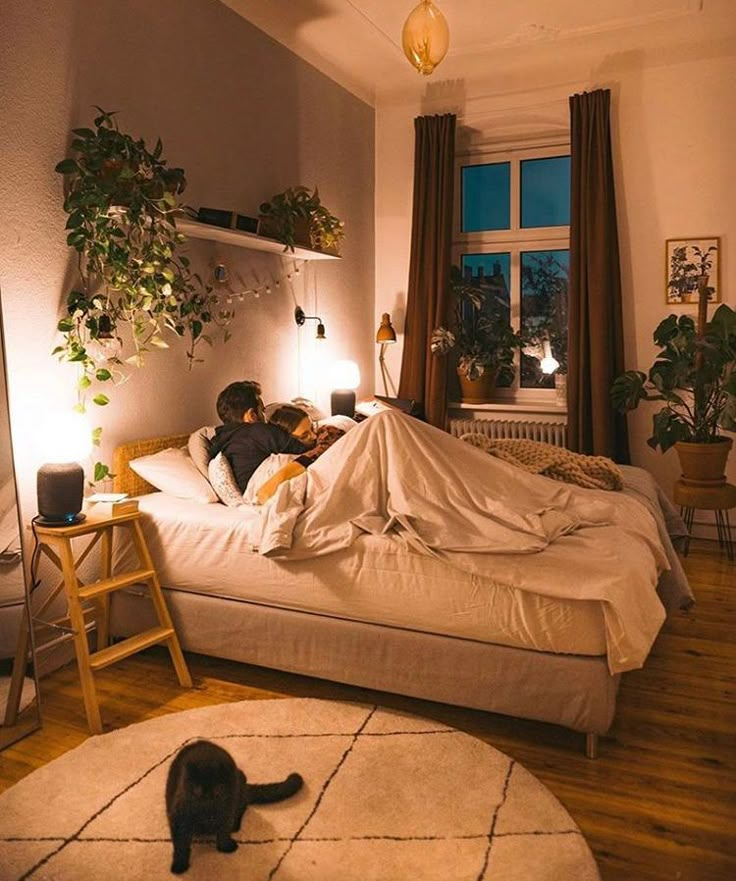 a person laying in bed with a cat on the floor next to them and a lamp