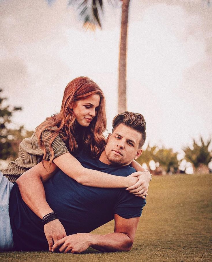 a man and woman are laying on the ground in front of a palm tree, with their arms around each other