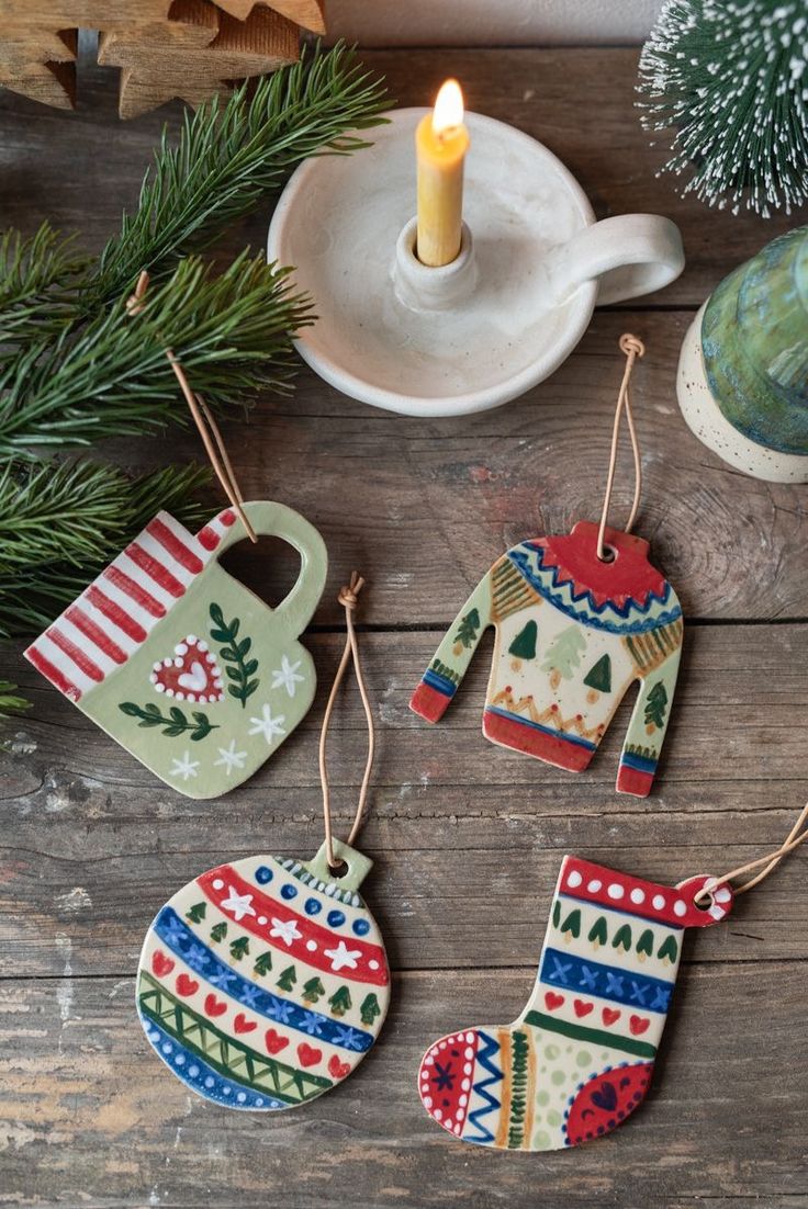 three ornaments are hanging on a wooden table next to a candle and some pine branches