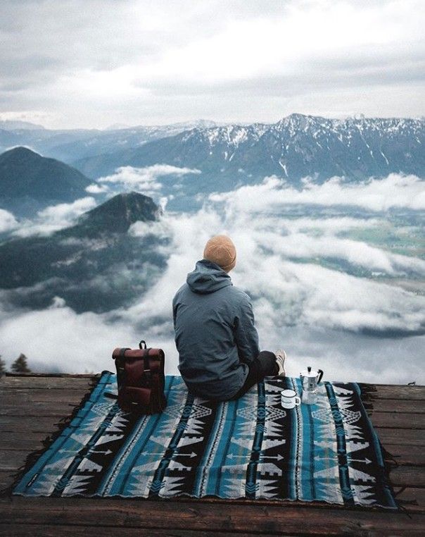 a man sitting on top of a wooden floor next to a blanket with mountains in the background