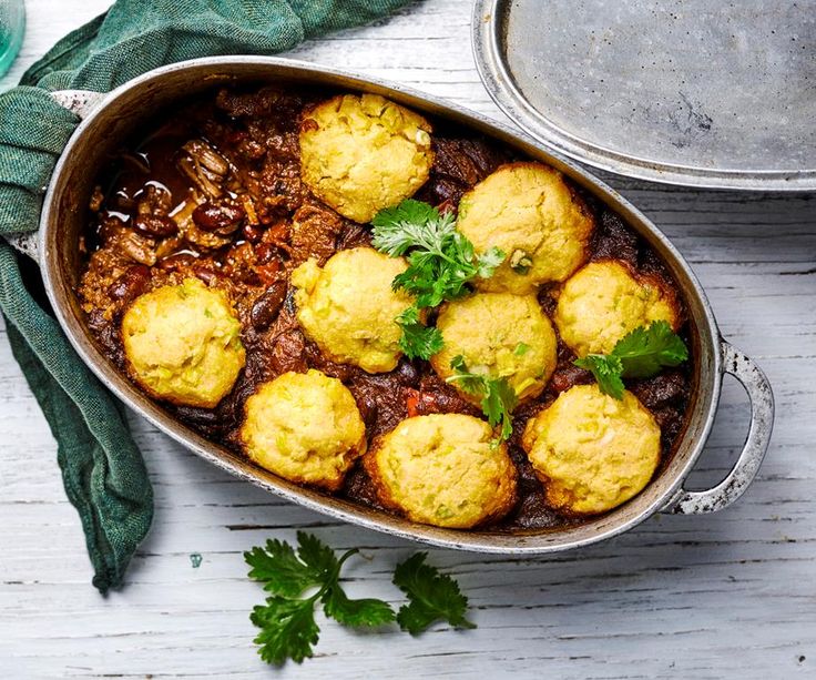 a pan filled with meat and dumplings next to a pot of sauce on a table