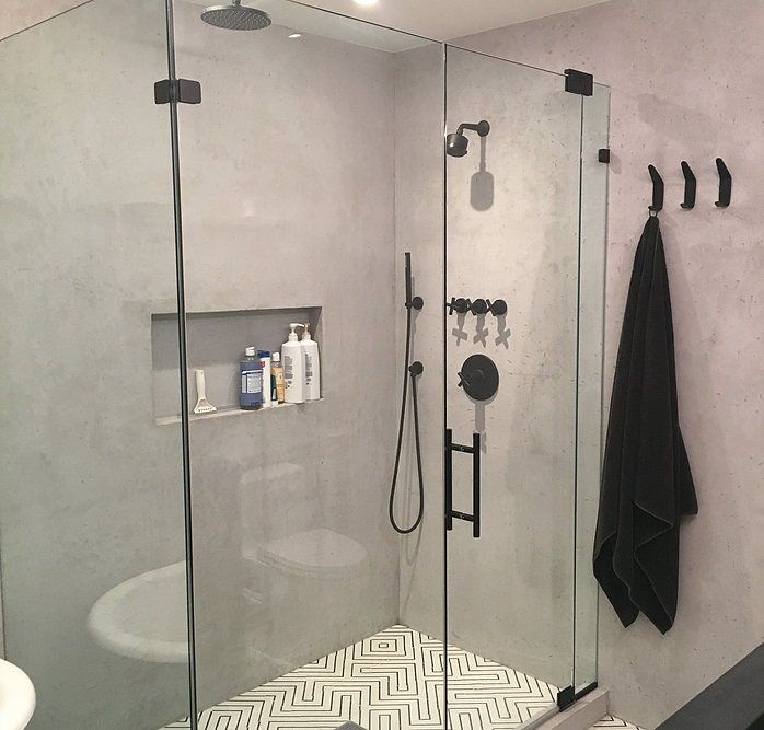 a walk in shower sitting next to a white sink and black towel on the wall