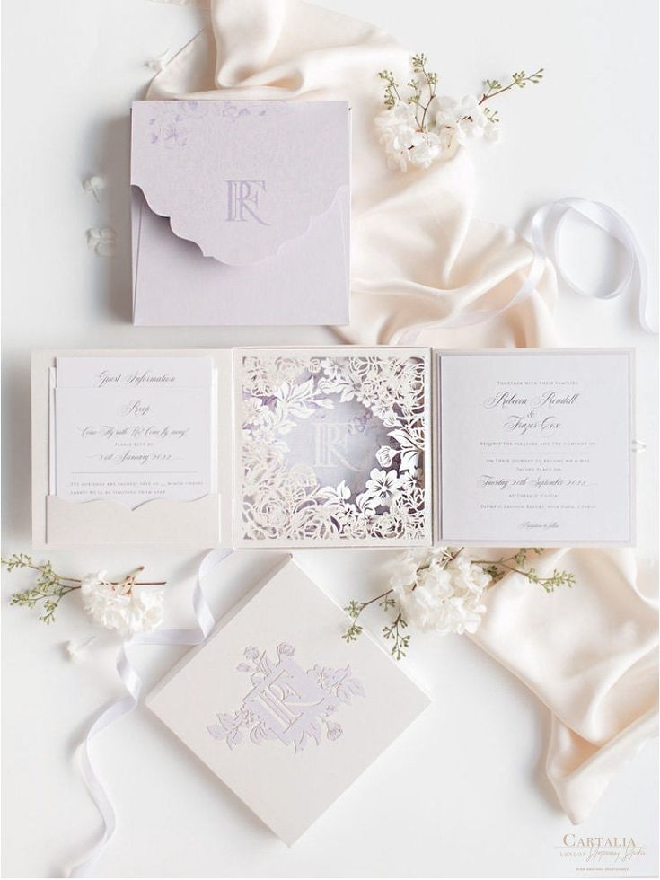 the wedding stationery is laid out on top of white satin, with flowers and ribbons