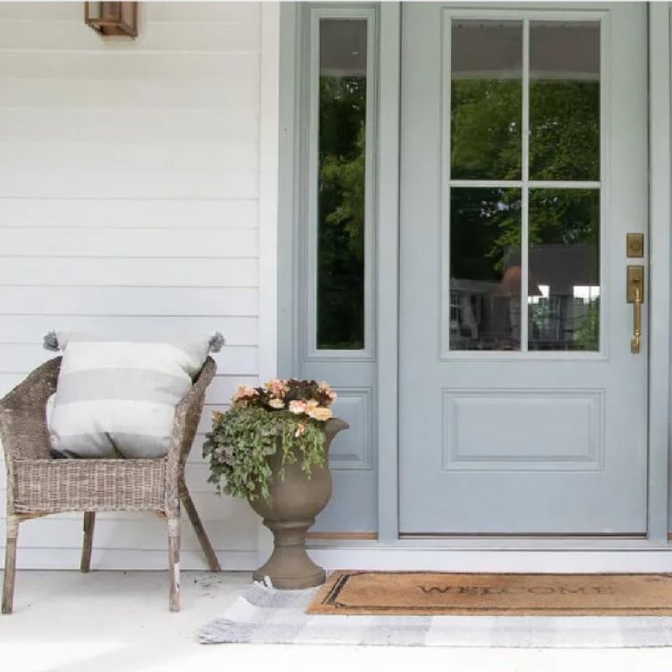 two chairs sitting on the front porch of a house with blue doors and white walls