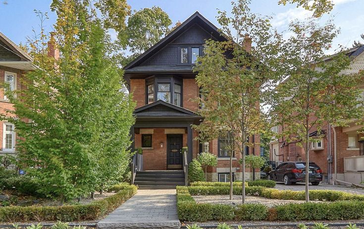 a house with many trees in front of it and bushes on the sidewalk next to it