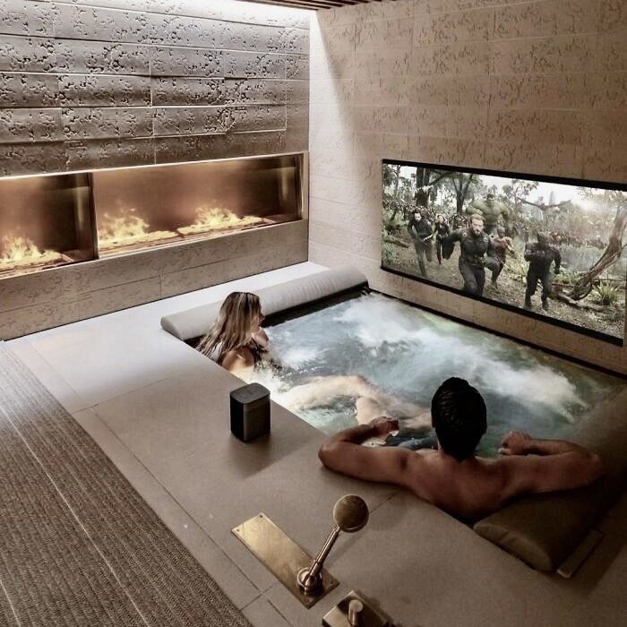 a man and woman are sitting in an indoor hot tub with fireplaces on the wall