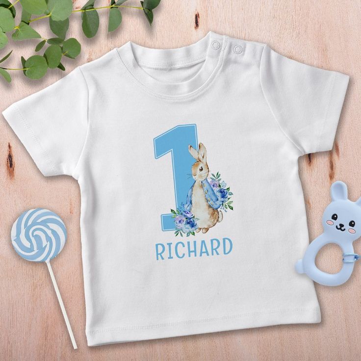 Watercolor Blue Peter Rabbit Baby Boy's First Birthday Baby T-Shirt. Matching items available. Blue Crew Neck Top For First Birthday, Blue Summer T-shirt For First Birthday, Blue Graphic Print T-shirt For First Birthday, Blue Cotton T-shirt For First Birthday, Blue Crew Neck T-shirt For First Birthday, Blue Short Sleeve T-shirt For First Birthday, Blue Short Sleeve T-shirt, Blue Tops With Name Print For Birthday, Blue T-shirt With Name Print For Birthday