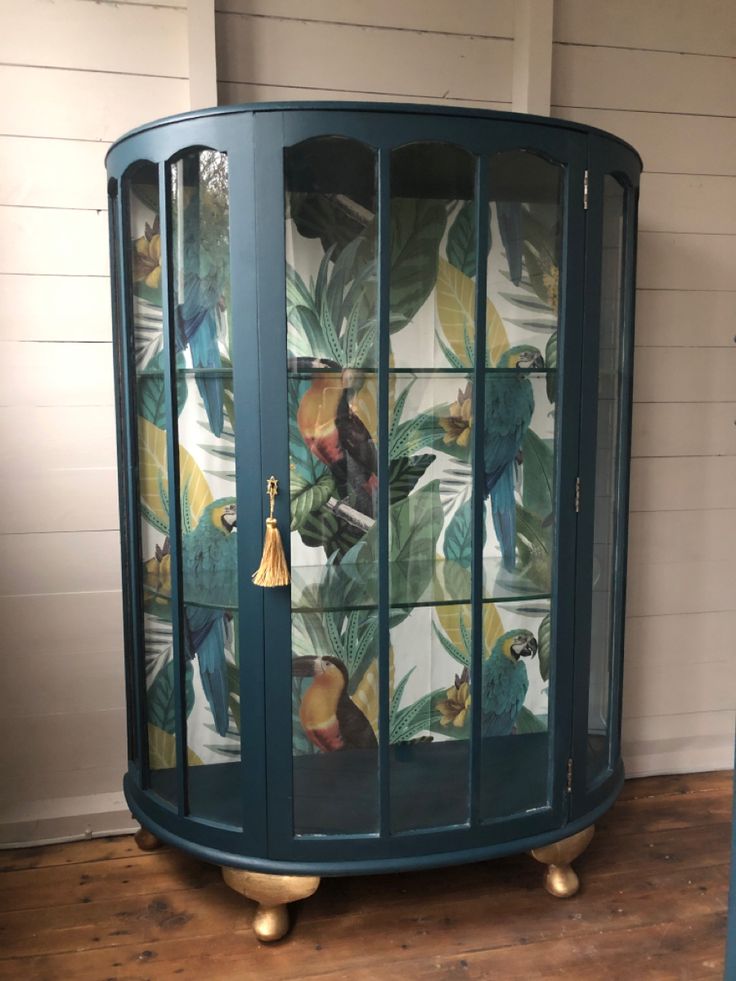 a green cabinet with birds and leaves on the glass doors is next to a wooden floor