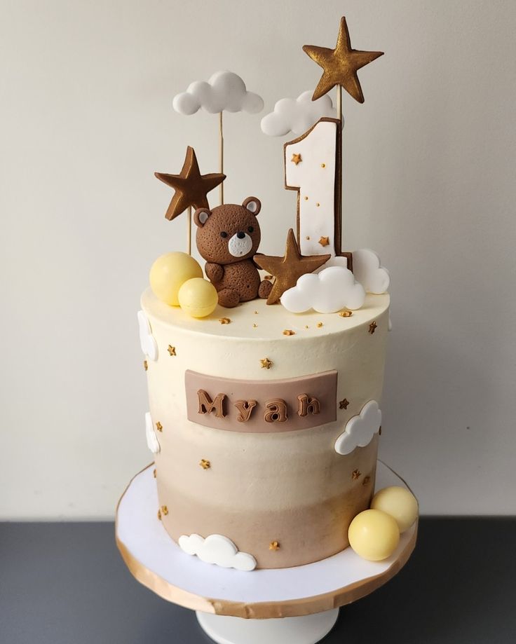 a birthday cake decorated with stars, clouds and a teddy bear sitting on the top