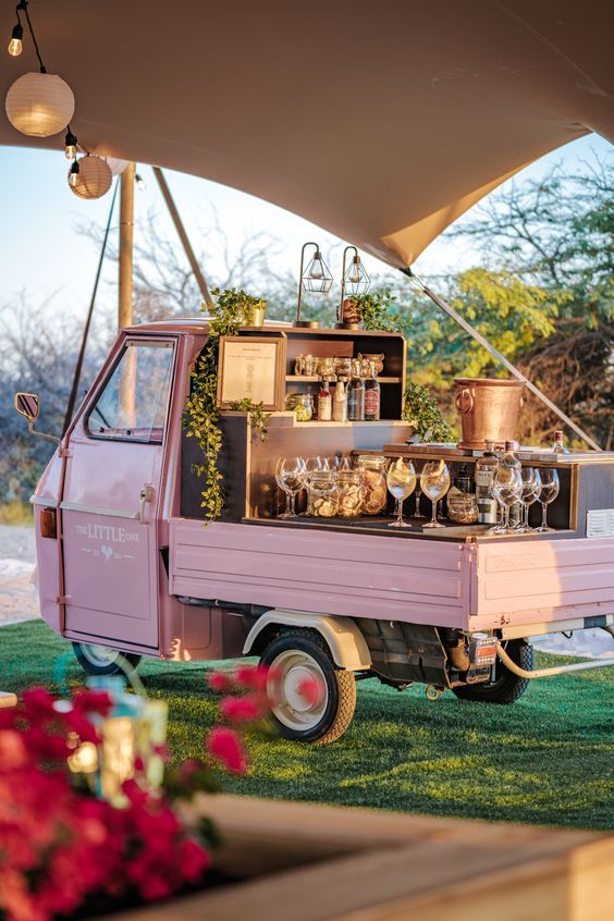 an old pink truck with wine glasses on the back parked in front of a tent