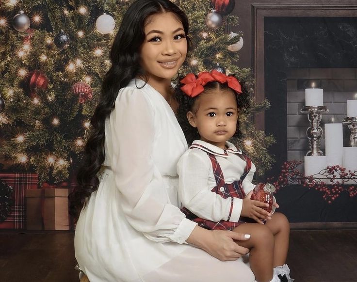 a woman holding a small child in front of a christmas tree