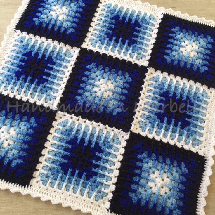 a blue and white crocheted afghan with squares on it, sitting on top of a wooden table