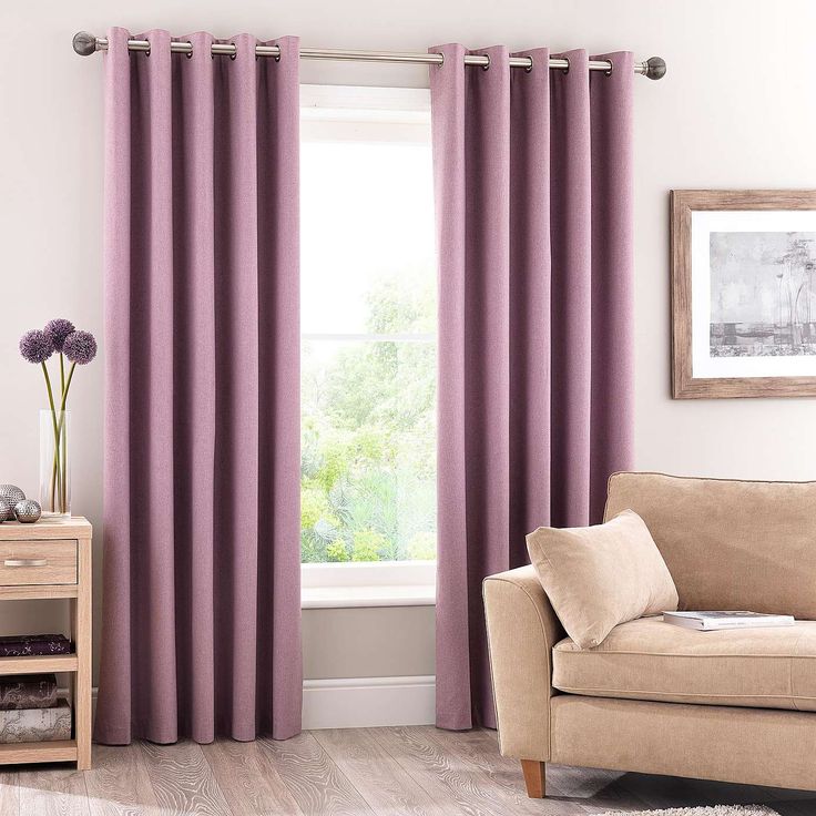 a living room with purple curtains and a beige couch in front of a window on a wooden floor