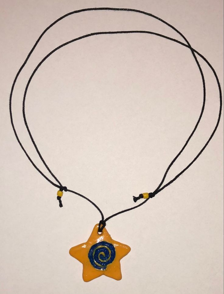 a yellow and blue star shaped necklace with a black cord around it on a white surface