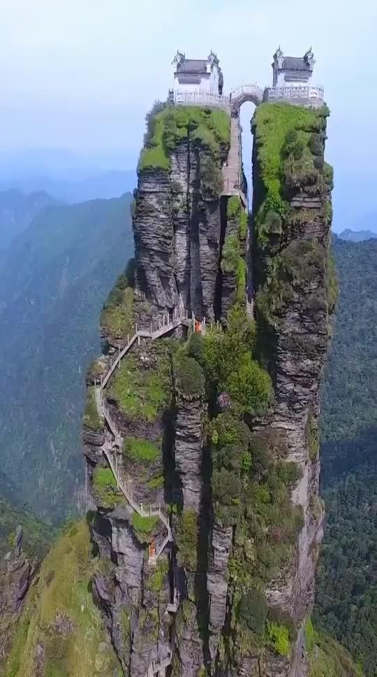 two tall rock towers with stairs on top of them, surrounded by greenery and mountains