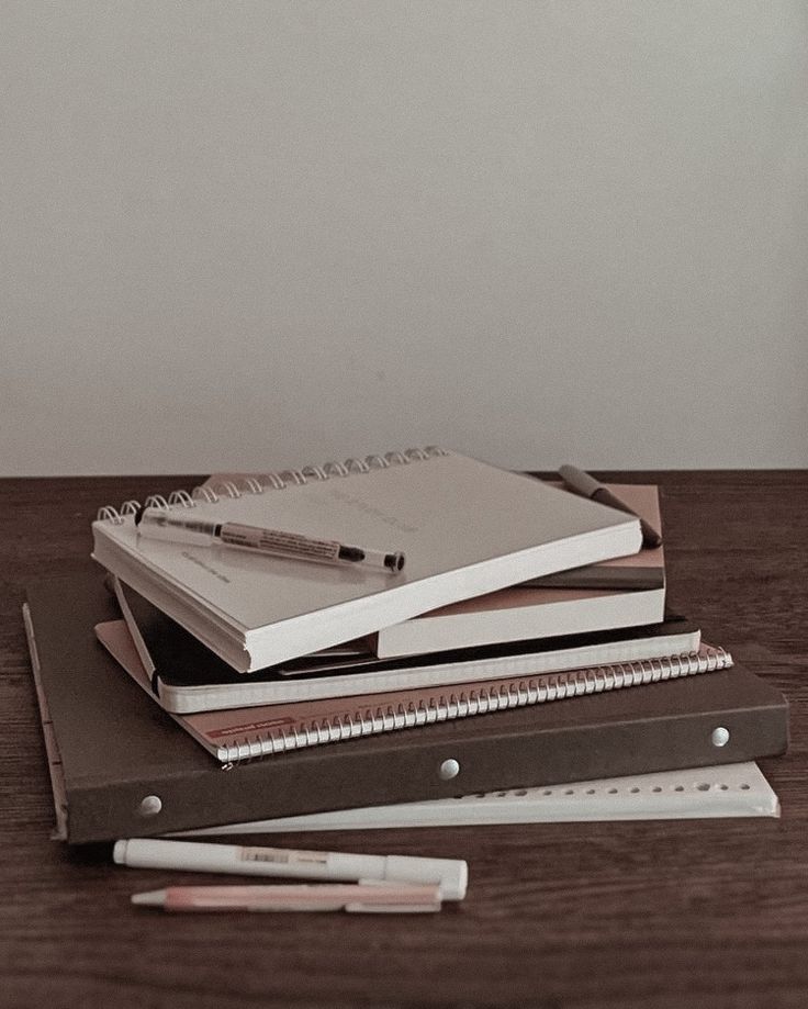 a stack of notebooks sitting on top of a wooden table next to a pen