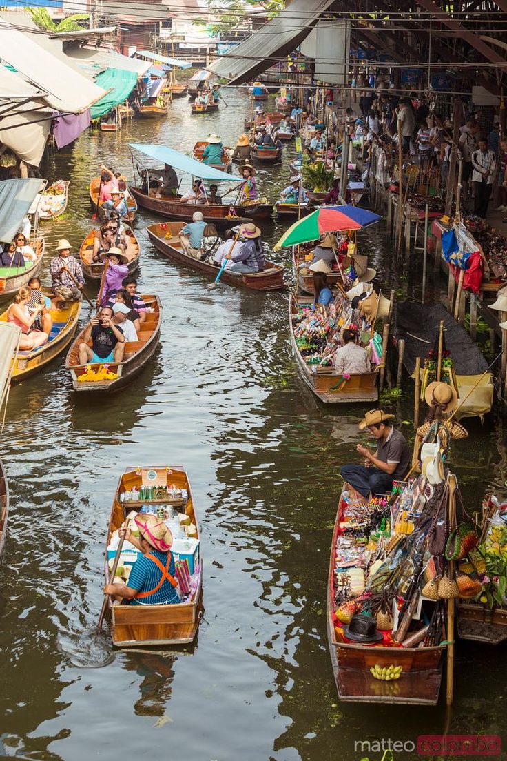 many small boats floating on top of a river filled with lots of people and umbrellas