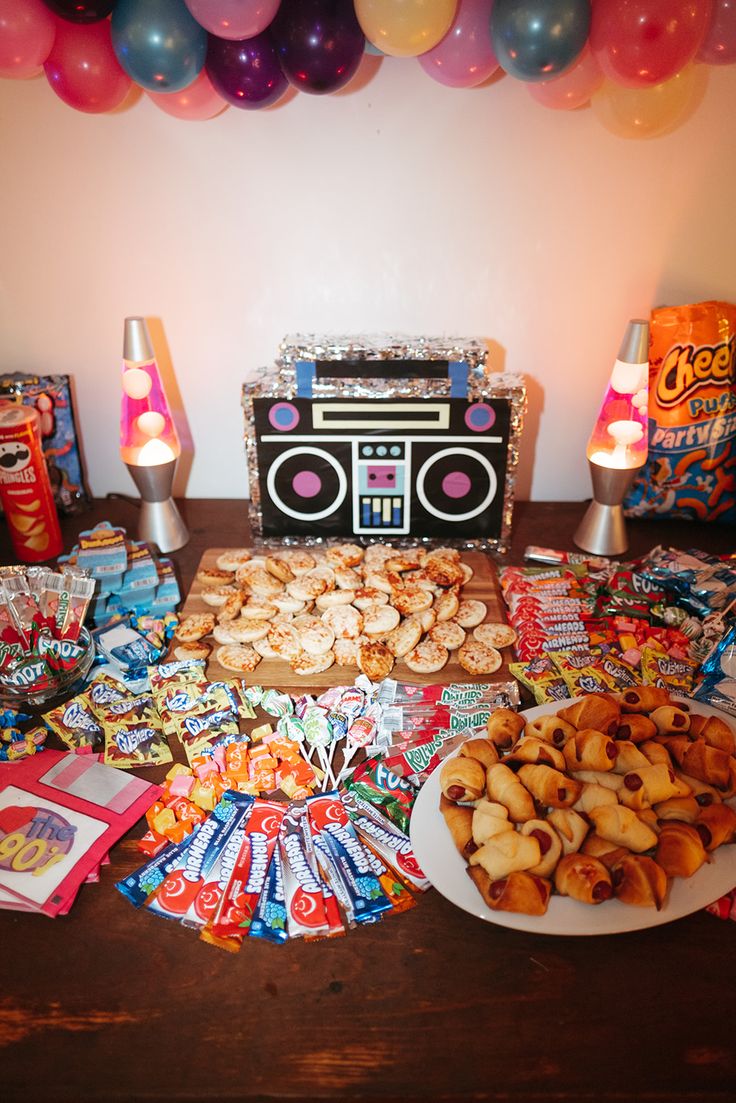 a table topped with lots of food and balloons next to a boombox filled with candy