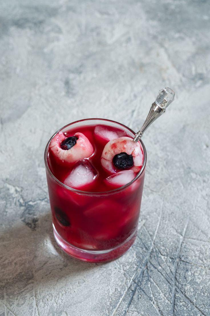 two glasses filled with ice and fruit on top of a table next to a spoon