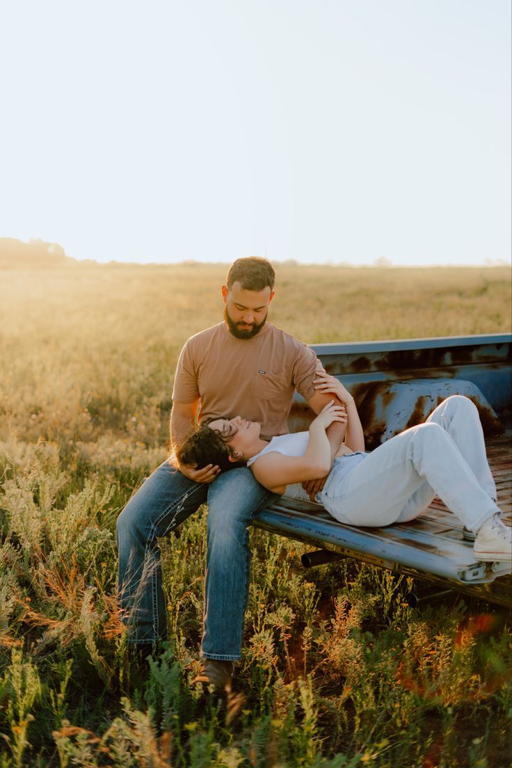 a man and woman sitting on the back of a pickup truck in an open field