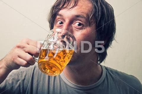 a man drinking beer from a glass in front of his face with eyes wide open