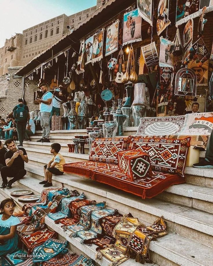 people are sitting on the steps in front of an outdoor market with rugs and other items