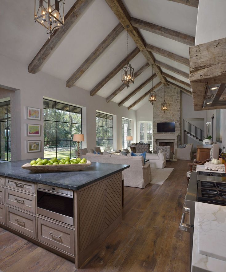 a large open concept kitchen and living room with wood flooring, exposed beams and stone fireplace