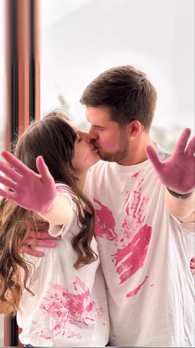 a man and woman kissing each other with their hands in the air while they are painted pink