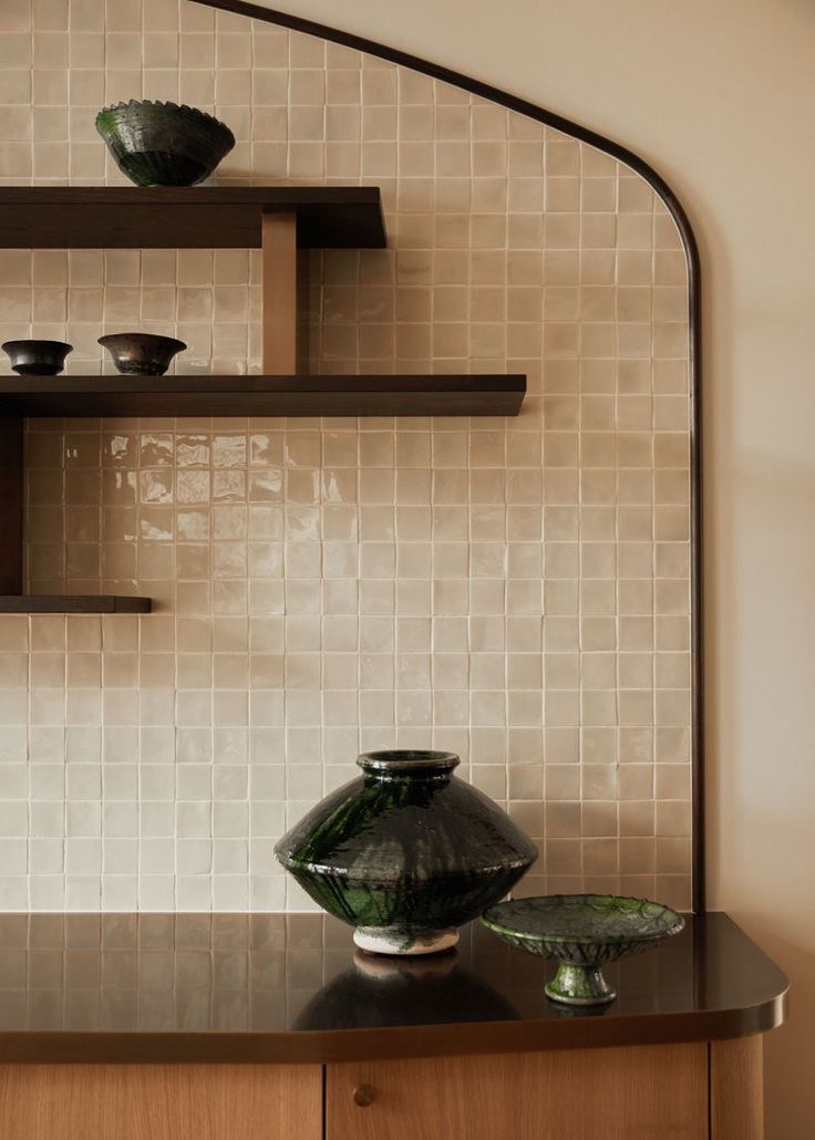 two green vases sitting on top of a wooden shelf next to a white tiled wall