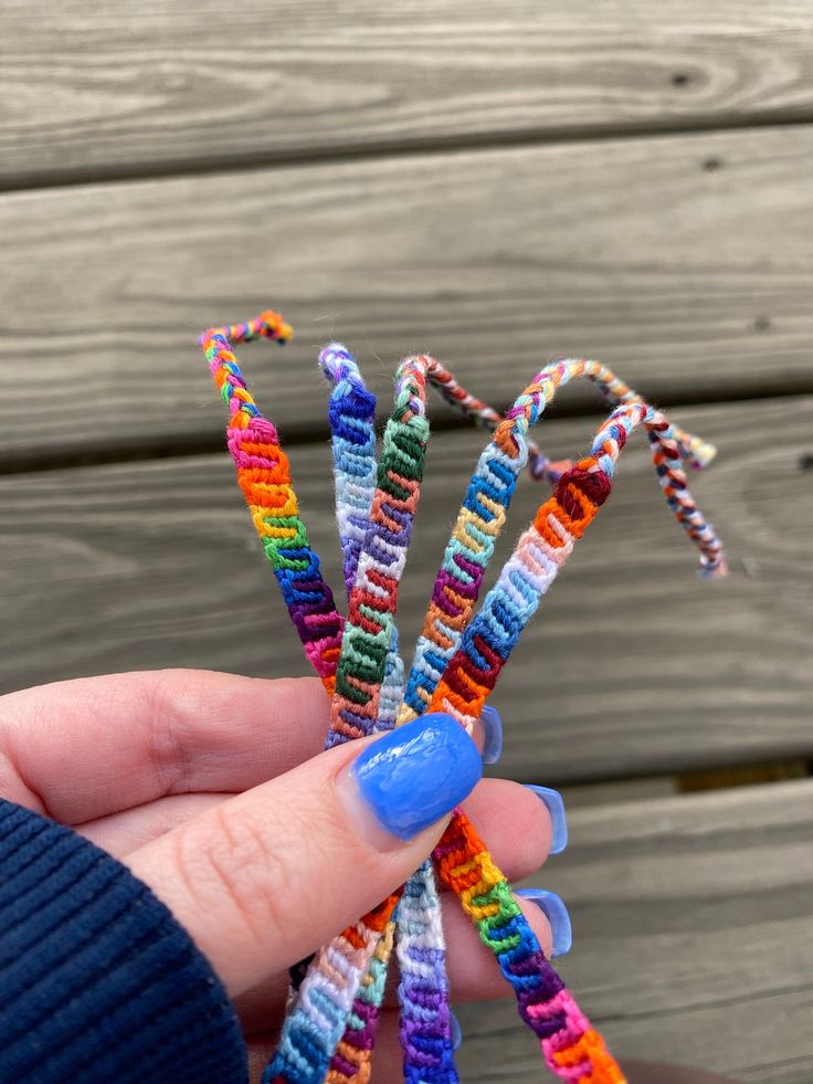 a person holding some colorful beads in their hand on a wooden surface with wood planks behind them