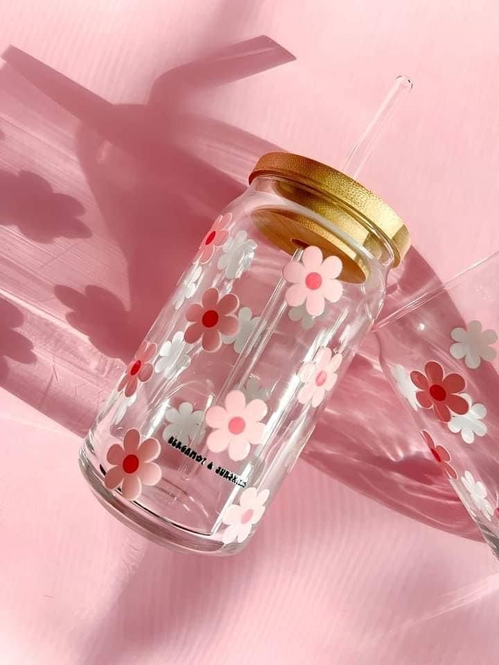 two glass jars with flowers painted on them sitting next to each other in front of a pink background