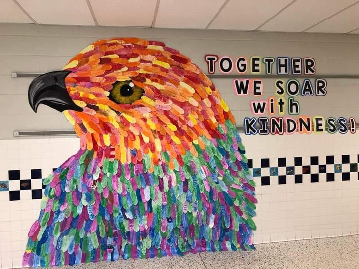 a colorful bird made out of plastic bottles in front of a sign that says together we soar with kindness