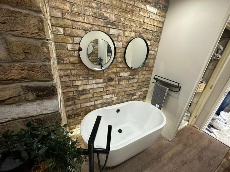 a white bath tub sitting next to a brick wall with three mirrors on it's side