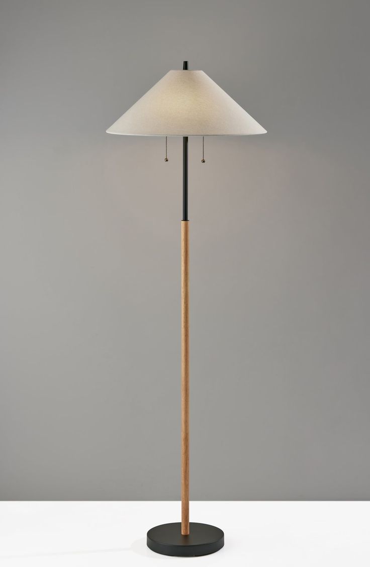 a floor lamp with a wooden base and a white shade on the top of it