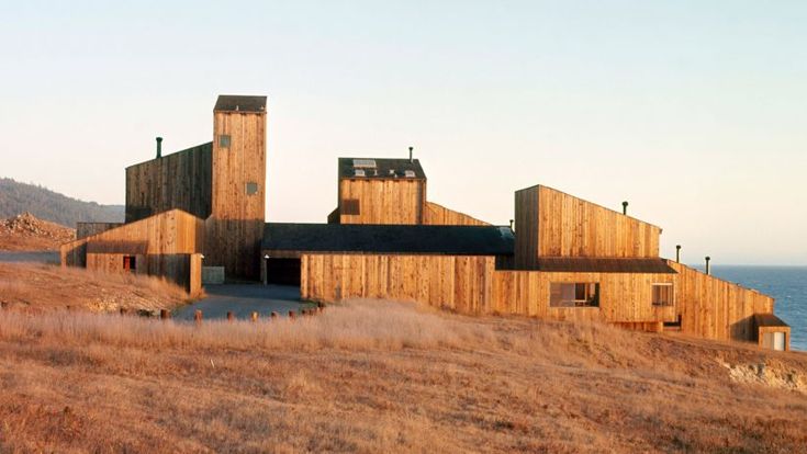 an abandoned building sits in the middle of a grassy field with water and mountains in the background