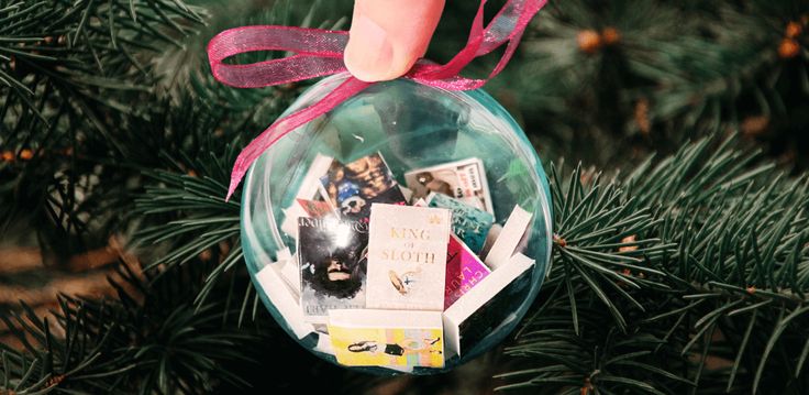 a hand is holding an ornament with pictures in it on a christmas tree