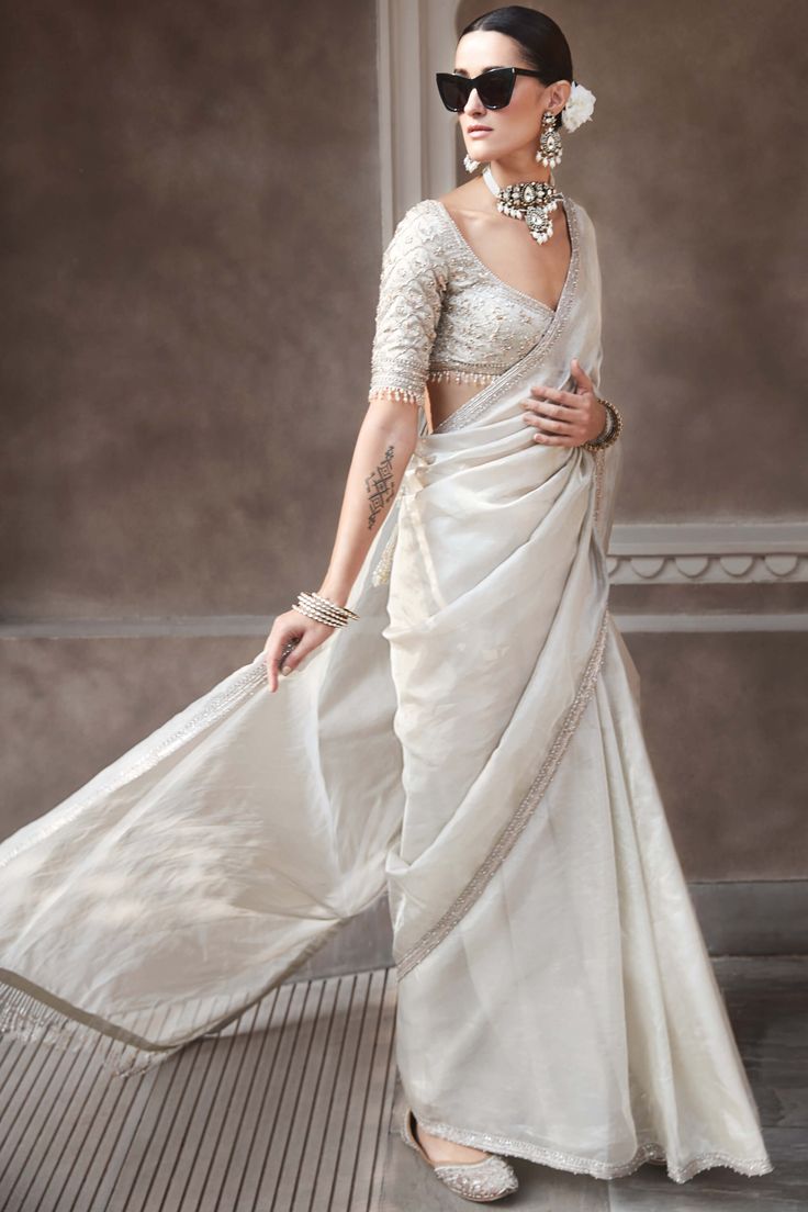 The silver needle sari elevates the classic Indian silhouette with a celestial update. The blouse is inspired by the moon, adorned with small crescents on the sleeves. The silver wrinkled tissue sari features rustic zardozi pittan over silk and anmol dori work, reflecting understated elegance. Silver Tissue Saree, Silver Blouse Designs For Saree, Traditional Silver Blouse Piece For Eid, Silver Chanderi Traditional Designer Wear, Festive Silver Chanderi Blouse Piece, Silver Bollywood Saree For Festive Occasions, Elegant Silver Pre-draped Saree For Festive Occasion, Silver Pre-draped Saree With Cutdana For Festivals, Silver Wedding Blouse Piece With Sheer Dupatta