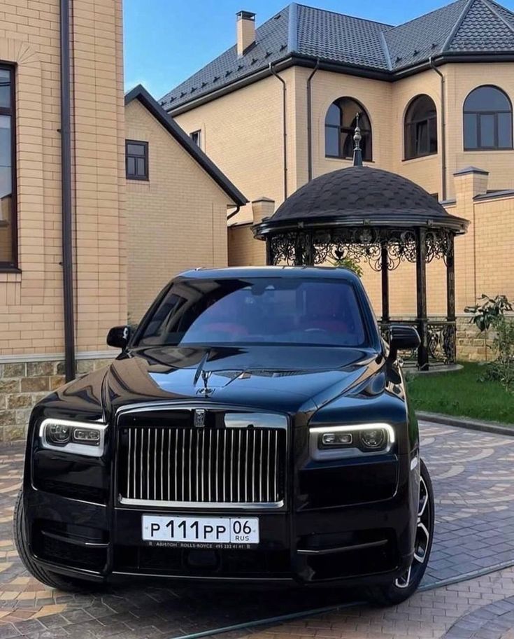 a black rolls royce is parked in front of a large house with a gazebo