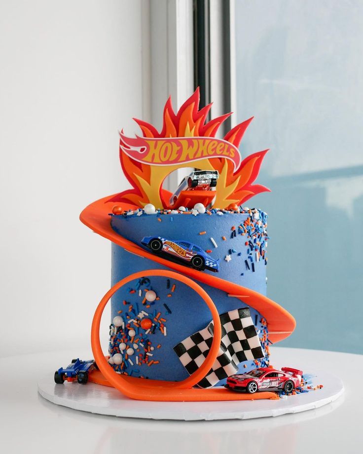 a birthday cake with cars and flames on the top is sitting on a white table