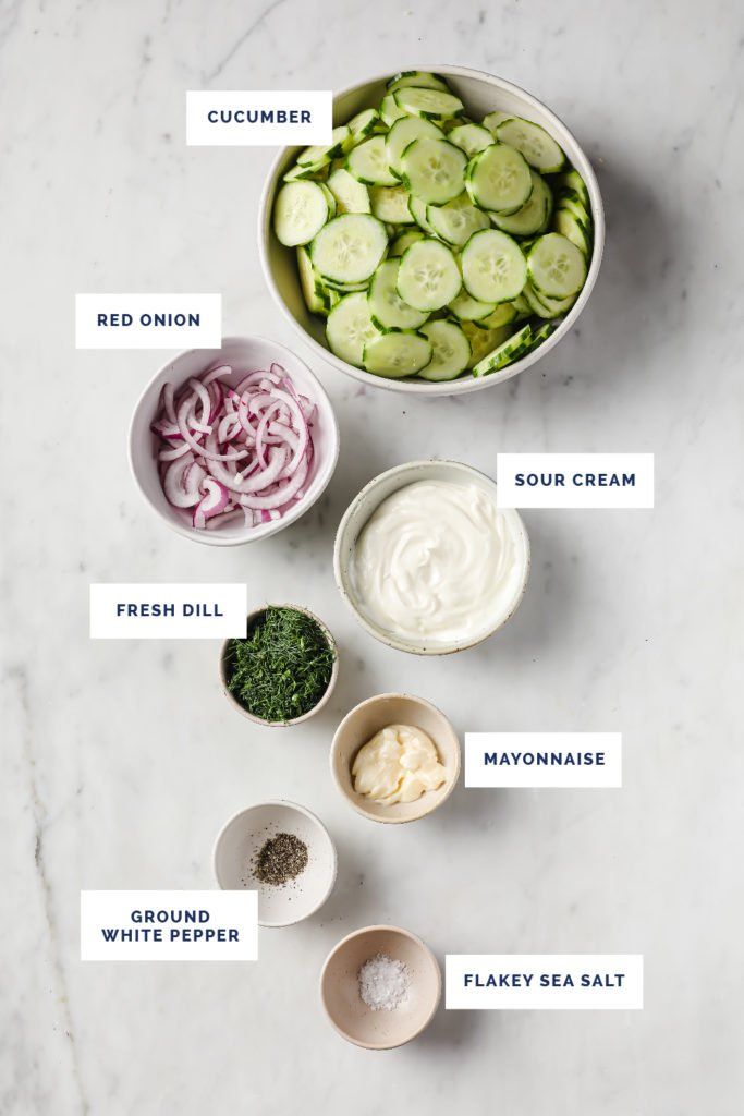 ingredients for cucumber salad laid out in bowls on a white marble counter top