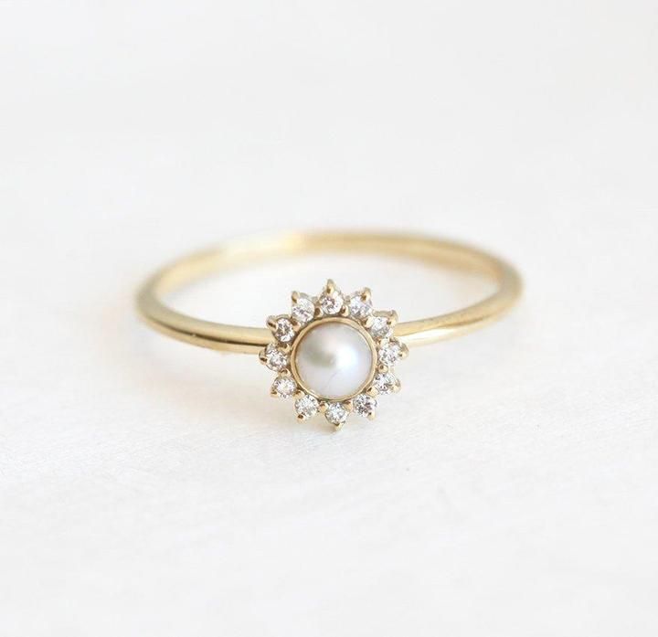 a gold ring with a white pearl and diamonds on the front, sitting on a white surface